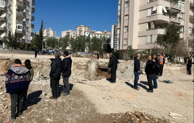 People gather at the site of a collapsed building in Adana