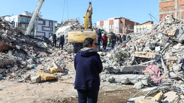 A woman stands in front of collapsed buildings following a powerful earthquake in Adiyaman, Turkey