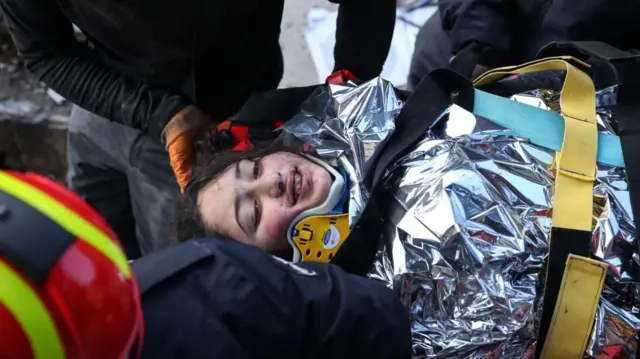 A child wrapped in foil blankets is rescued from rubble