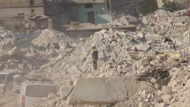 A White Helmet volunteer stands among rubble in Harem, Syria