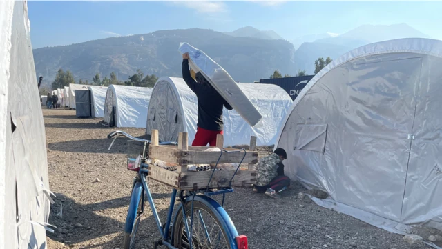 A man carries a mattress through rows of tents