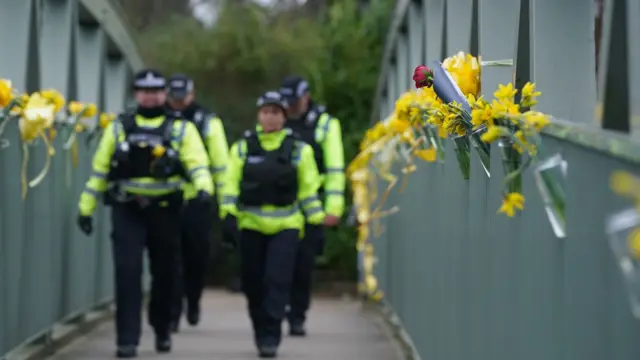 Police officers walk past yellow ribbons and messages of hope tied to a bridge for Nicola Bulley over the River Wyre