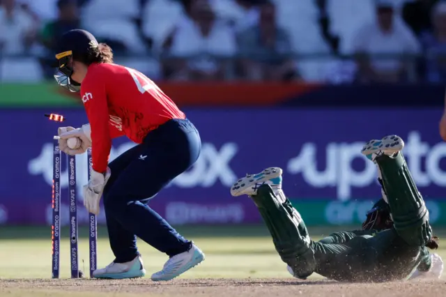 Pakistan's Tuba Hassan (R) slides to make it back to the crease as England's wicketkeeper Amy Jones (L) unsuccessfully attempts to run her out during the Group B T20 women's World Cup cricket match between England and Pakistan at Newlands Stadium