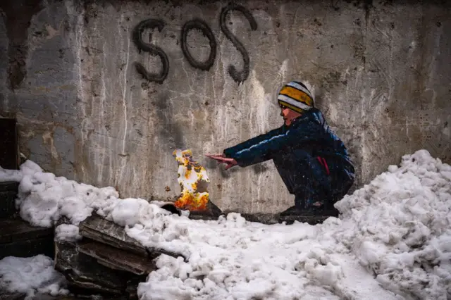 A mural depicting a boy warming his hands by a fire on the ground