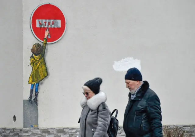 A mural on the side of a building showing a young girl painting the word "war" on a "stop" sign