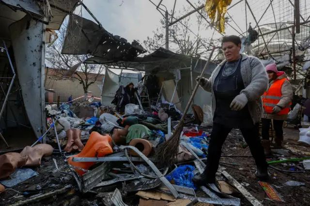 A woman holding a broom walks down a debris covered street