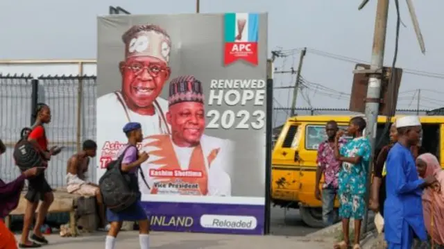 People walk past an electoral campaign poster of All Progressives Congress (APC) Presidential candidate, Bola Tinubu