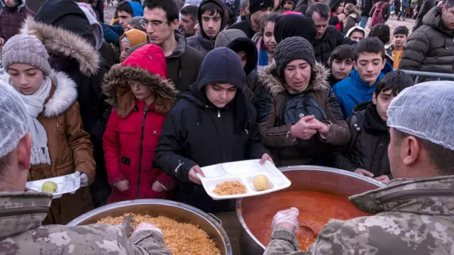 Children receive hot food while a large queue forms behind them in Diyarbakir