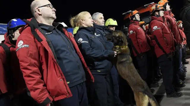 Emergency workers and a service dog wait in a line