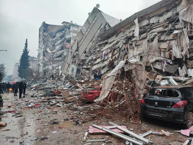 People stand in front of collapsed buildings following an earthquake in Kahramanmaras, Turkey