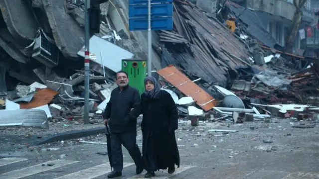 People walk past a collapsed building after the earthquake in Kahramanmaras, Turkey