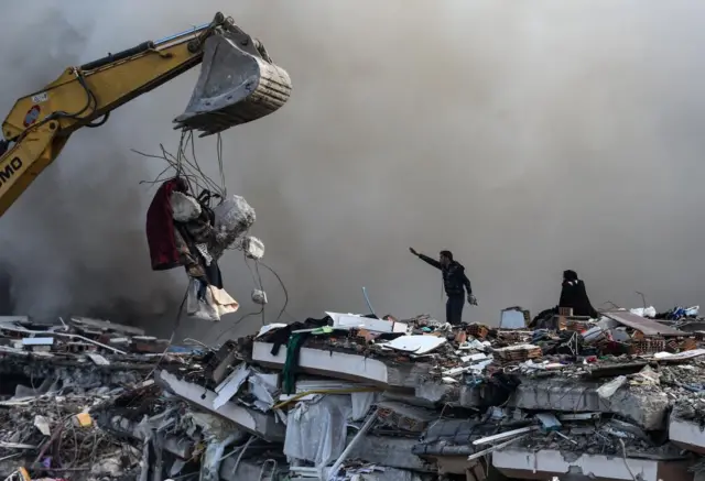 A man and digger search through rubble in Hatay