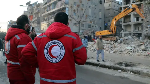 Two men wearing red crescent jackets look at damage