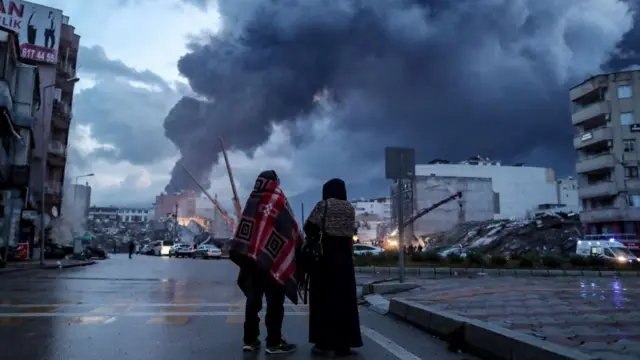 People wait near the site of a collapsed building after an earthquake in Iskenderun district of Hatay, Turkey