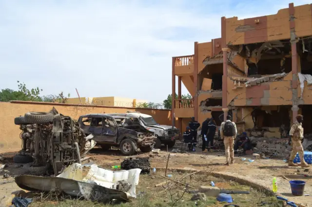 A Malian firefighters and soldiers walks beside a destroyed building and burnt cars on November 13, 2018