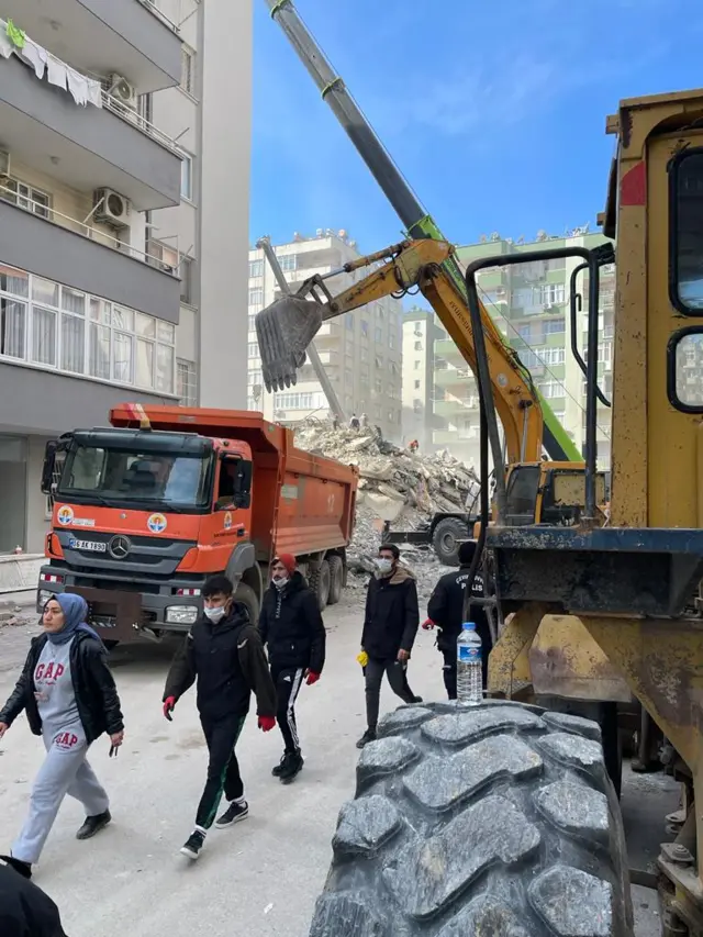 Rescue workers and lorries in front of the rubble of a 10-storey building in Adana, Turkey