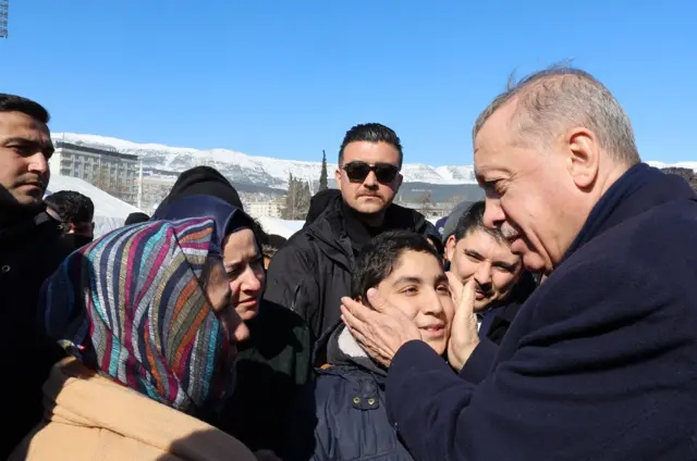 Turkish President Recep Erdogan speaks to people while visiting the city of Kahramanmaras in the aftermath of the February 2023 earthquake. He is seen with his hands on a boy's cheeks.