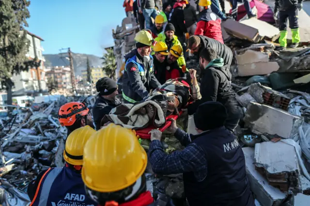 Members of a search & rescue team carry a survivor on a stretcher from a collapsed building in the city of Hatay, Turkey