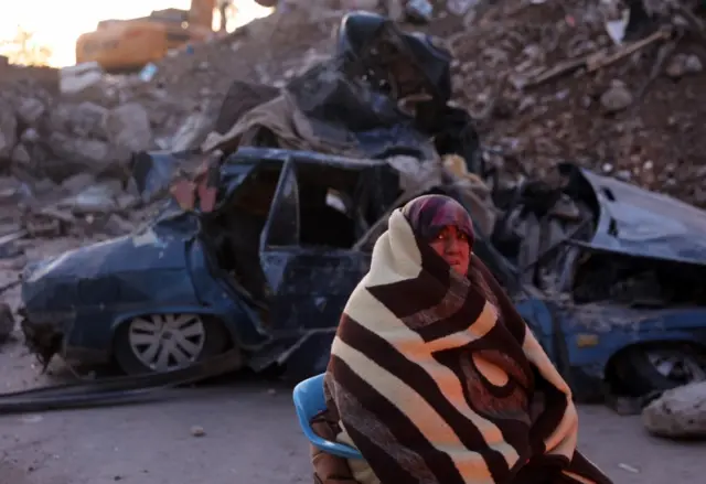 A woman siting next to collapsed buildings in the city of Kahramanmaras, southeastern Turkey,