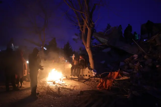 Survivors struggle to keep warm around a fire in the city of Kahramanmaras, southeastern Turkey