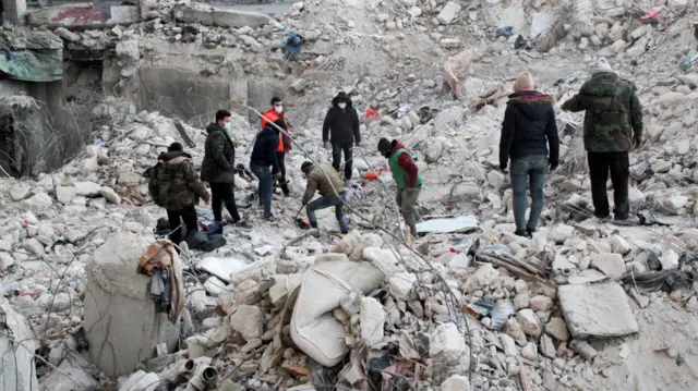 People stand on rubble as the search for survivors continues, in the aftermath of an earthquake, in Aleppo, Syria