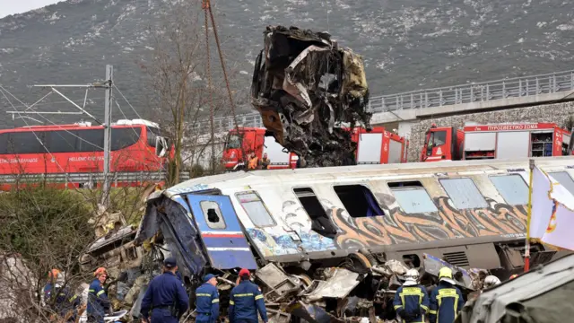 Crane vehicles try to remove pieces of damaged train wagons after the train collision