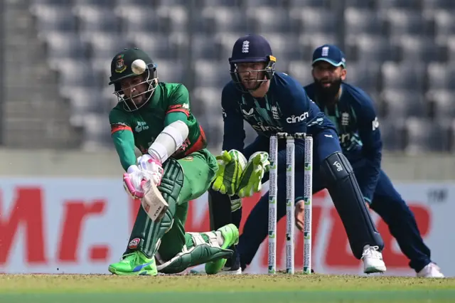 Bangladesh's Mushfiqur Rahim (L) plays a shot in front of England captain Jos Buttler (C) and Moeen Ali (L) during the first international one day cricket match between Bangladesh and England at the Sher-e-Bangla National Cricket Stadium