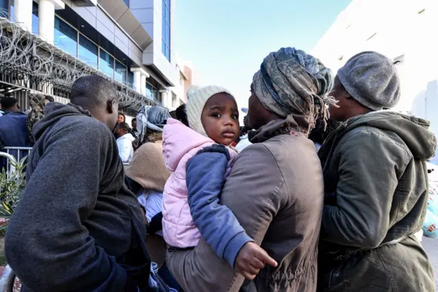 A child looks on while being carried by a woman as sub-Saharan African migrants wait outside the officers of the United Nations High Commissioner for Refugees (UNHCR) in Tunis