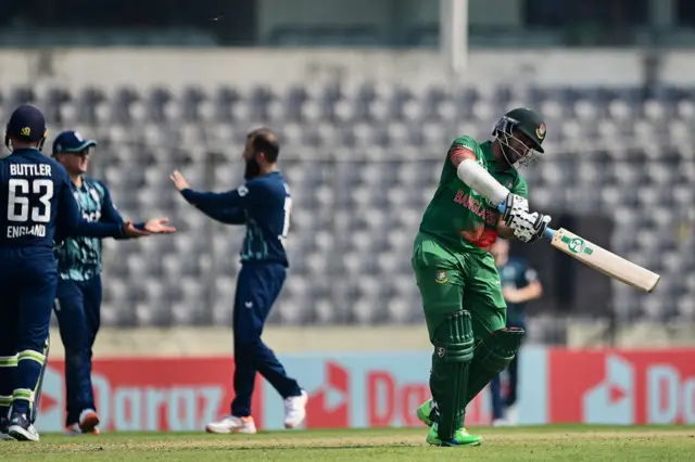 Bangladesh's Shakib Al Hasan (R) walks off the field after he was clean bowled by England's Moeen Ali (C) during the first international one day cricket match between Bangladesh and England at the Sher-e-Bangla National Cricket Stadium