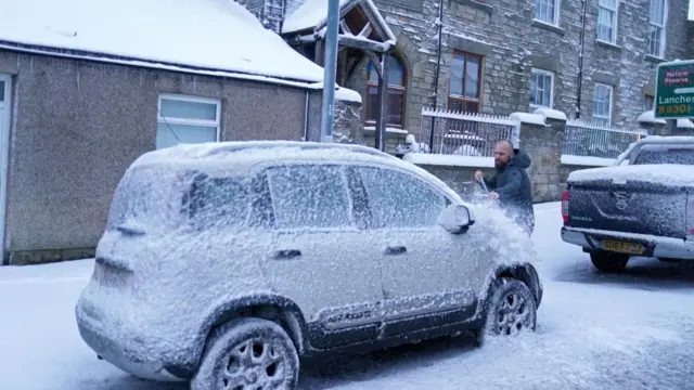 A man clears snow off his car in Court Durham