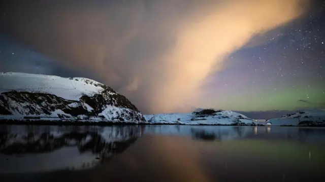 A hint of the aurora above the snow capped hills, with a shower cloud in the sky