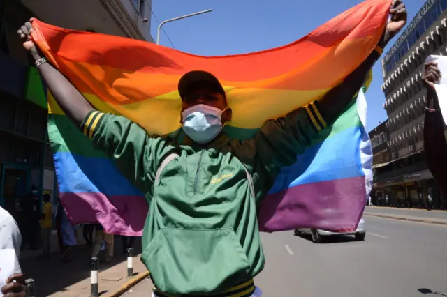 A demonstrator is seen holding an LGBTQ flag