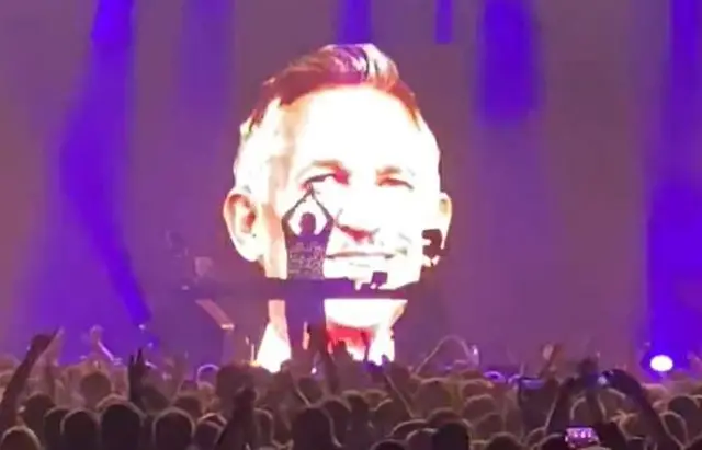 Crowds clap as a giant Gary Lineker photo appears during a gig