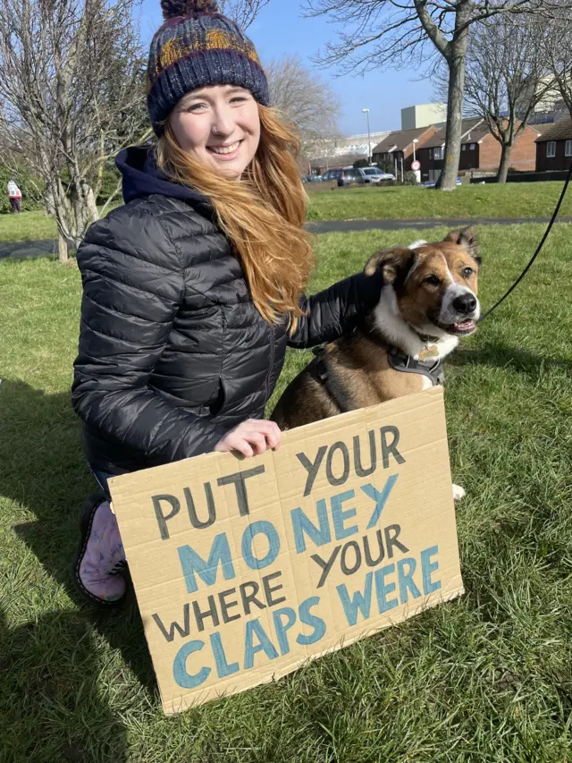 A woman holding a sign with a dog next to her