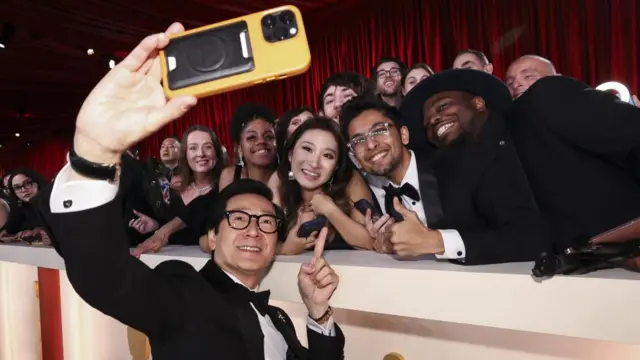 Ke Huy Quan poses on the champagne-colored red carpet during the Oscars arrivals