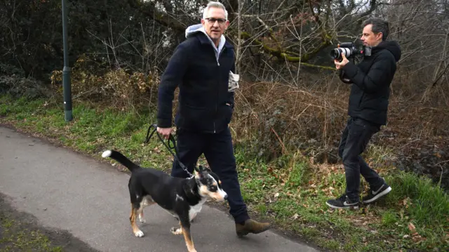 Gary Lineker walks his dog along a pavement alongside a photographer