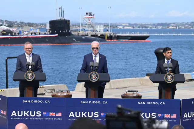 The three leaders stand at podiums at a US navy base by the port in San Diego, California