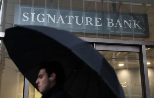 A man with an umbrella walks past a Signature Bank branch in New York