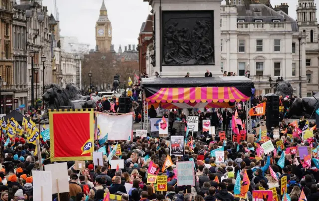 People on strike march through Trafalgar Square waving banners