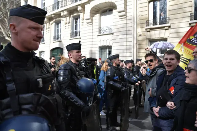 Protesters participate in a demonstration as nearby riot police officers