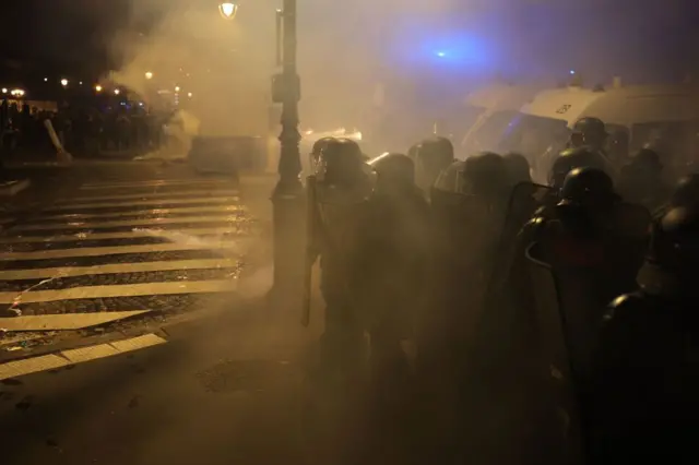 A group of riot police line up with shields and helmets