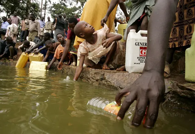 Pilgrims fill bottles with water from the pond near Namugongo