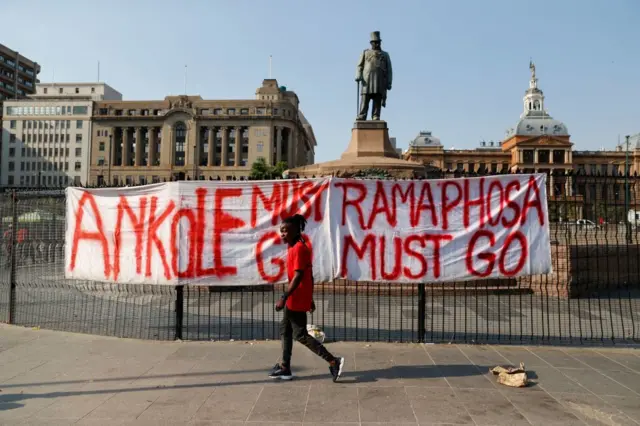 A member of the the Economic Freedom Fighters (EFF) walks past a banner that reads "Ramaphosa must go