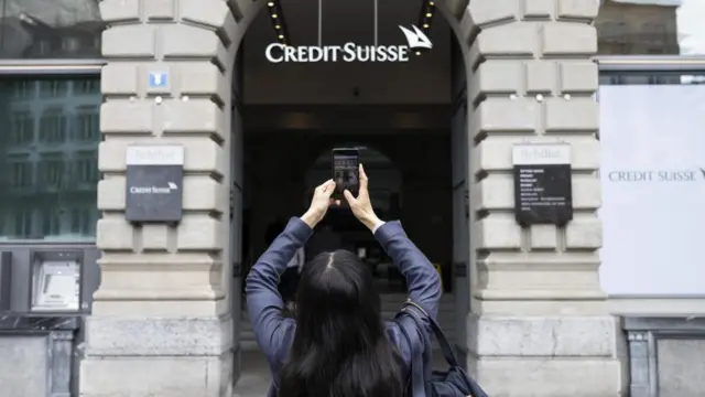 A woman takes photos of a logo of the Swiss bank Credit Suisse in Zurich, Switzerland