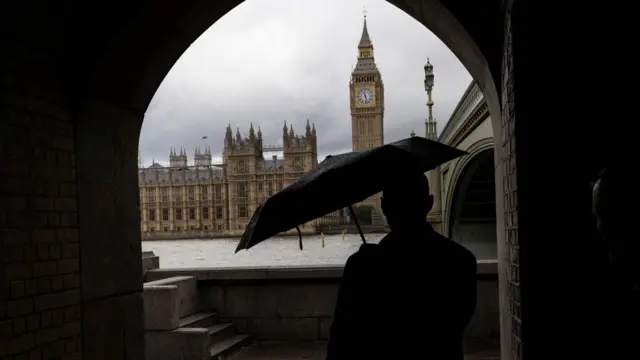 Stock image of the Houses of Parliament with a man with an umbrella in the foreground