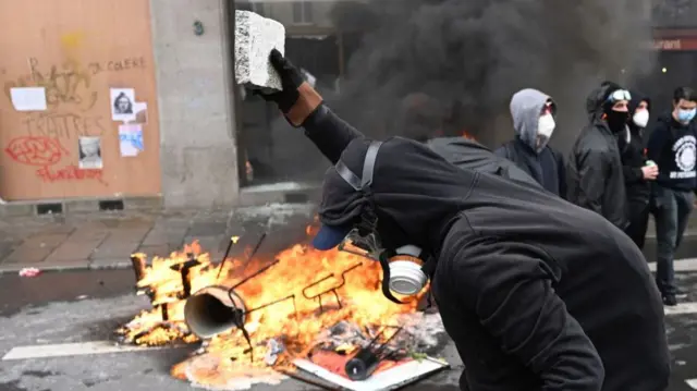 A demonstrator stands near burning wreckages during a rally against the law reforming the pensions system in Rennes, western France on March 23, 2023