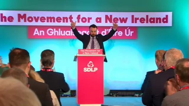 Colum Eastwood raises his arms as SDLP members applaud his speech