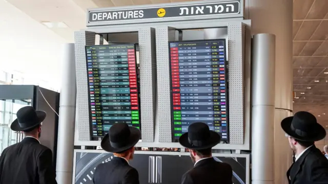 Four men in black hats look at departures board at Ben Gurion Airport, israel