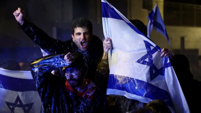 Protester punches fist into the air while holding Israel flag