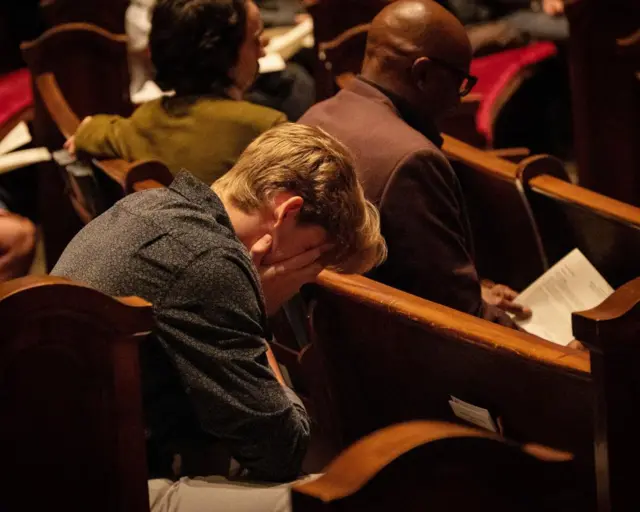 Mourner puts their head in their hands at a memorial